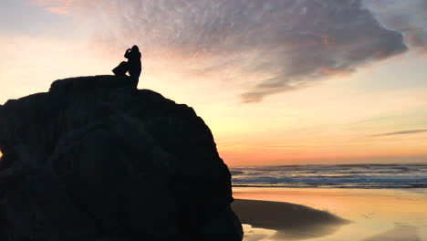 silhouette of two girls on a rock at bandon beach, one taking photos of the sunset