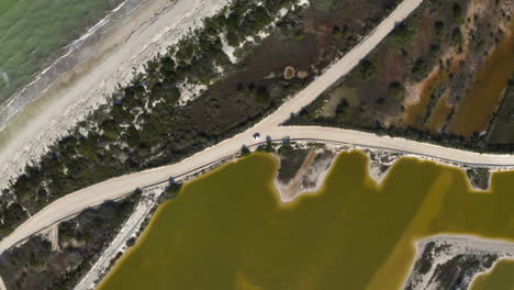 Car-driving-on-coastal-sandy-road-between-sea-and-murky-yellow-ponds