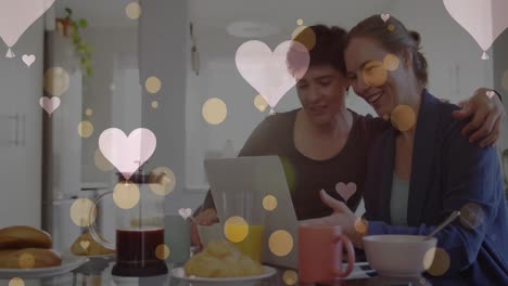 animation of hearts over caucasian female couple using laptop