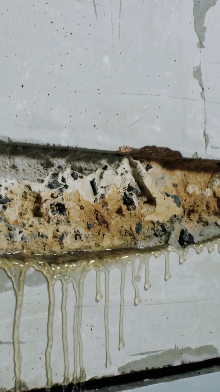 Vertikal video: Beskadiget samling siver fra råd på et metalpanel, viser smuldrende skum og ravfarvede dryp.