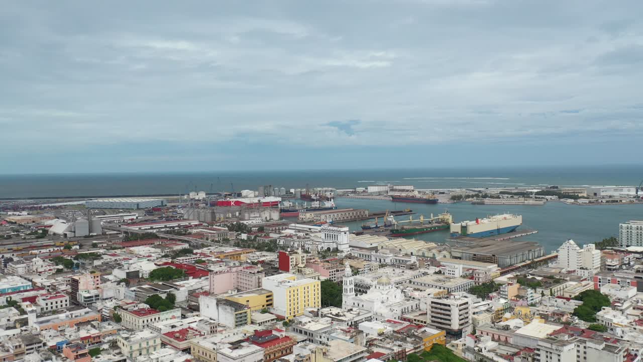 Aerial lateral shot of the Port of Veracruz, Mexico, showcasing cargo ships, industrial facilities, and the historic city center in the foreground as the drone moves sideways along the coastline