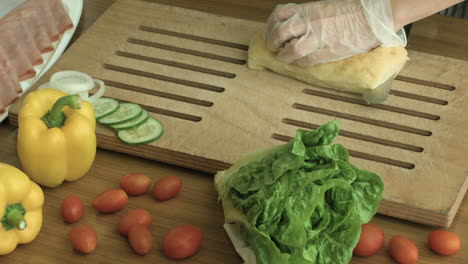 slicing a bread in a chopping board with vegetables and ham