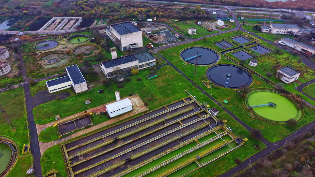 View of a wastewater treatment facility with large tanks and green areas in the city showing infrastructure and landscape in late afternoon light