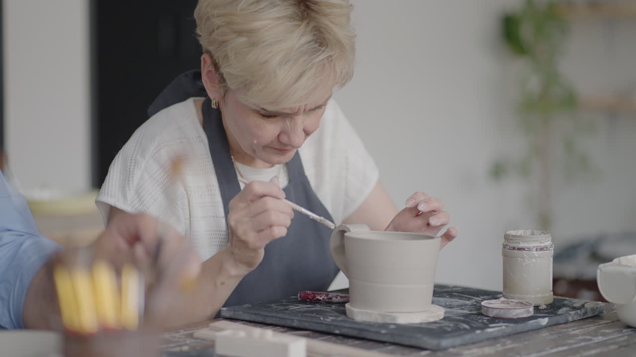 여성 도자기가 세라 ⁇  스튜디오에서 컵에 손잡이를 부착합니다. 여성 도자기가 도자기 작업실 스튜디오에서 컵을 형성하고 조각합니다.