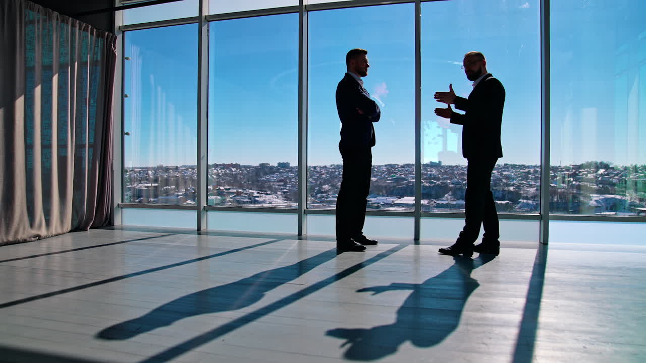 Business conversation of two man. Entrepreneurs in suits talking about business in spacious office room on windows backdrop.