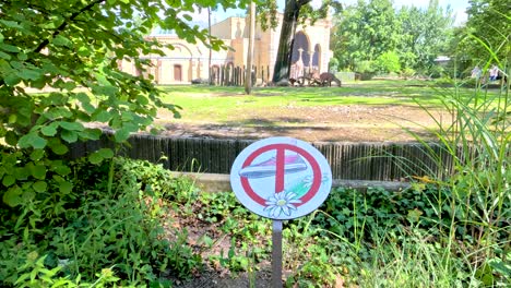 camera pans across a lush, sunlit park area in berlin, focusing on a no entry warning sign surrounded by greenery near a zoo enclosure