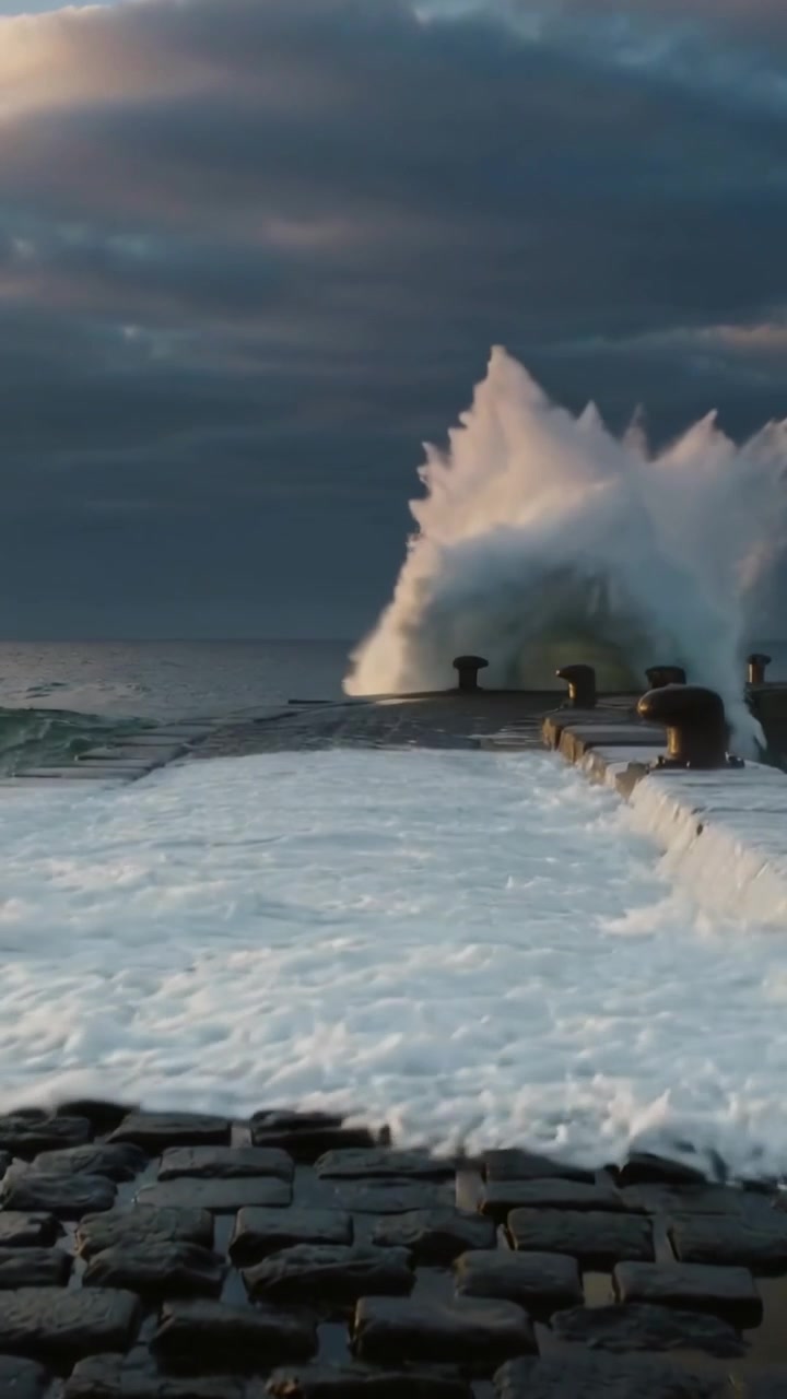 Vertical video: Surging swell driven by wind pushing water over stone pier, hitting metal bollards