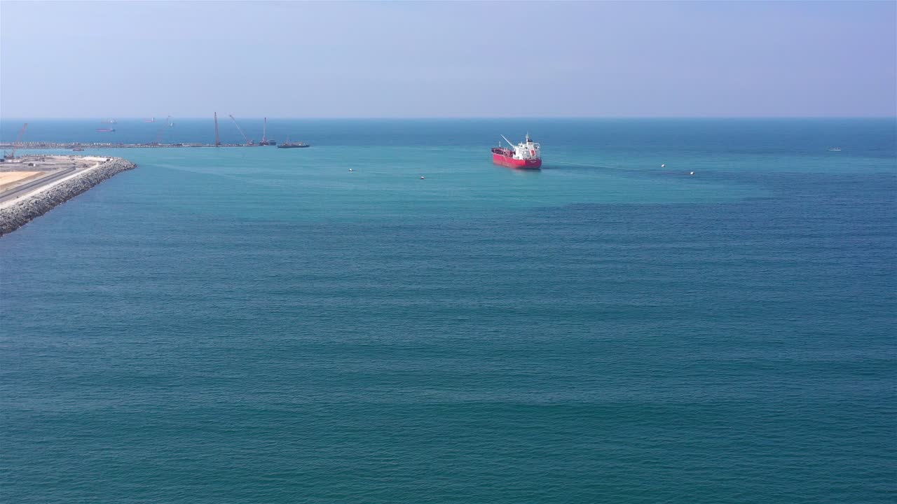 Red Cargo Ship Sailing in Blue Ocean Waters Near a Port or Construction Site