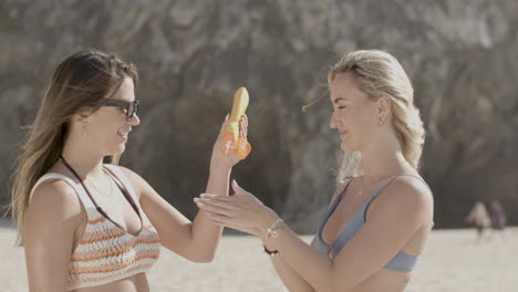 girl in bikini helping friend to apply sunscreen on shoulders