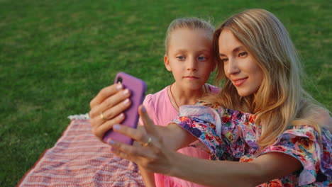 mother and daughter posing in park. family taking selfie on cellphone outdoor.