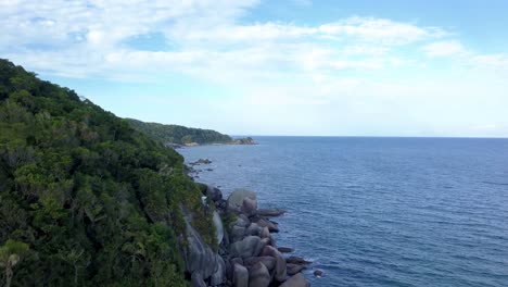 Aerial-jib-up-shot-of-the-rocky-coastline-with-hills-and-vegetation-near-Bombinhas,-Brazil