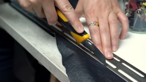 female hands cutting leather segment for crating a handbag using a guide spacer, handheld closeup shot