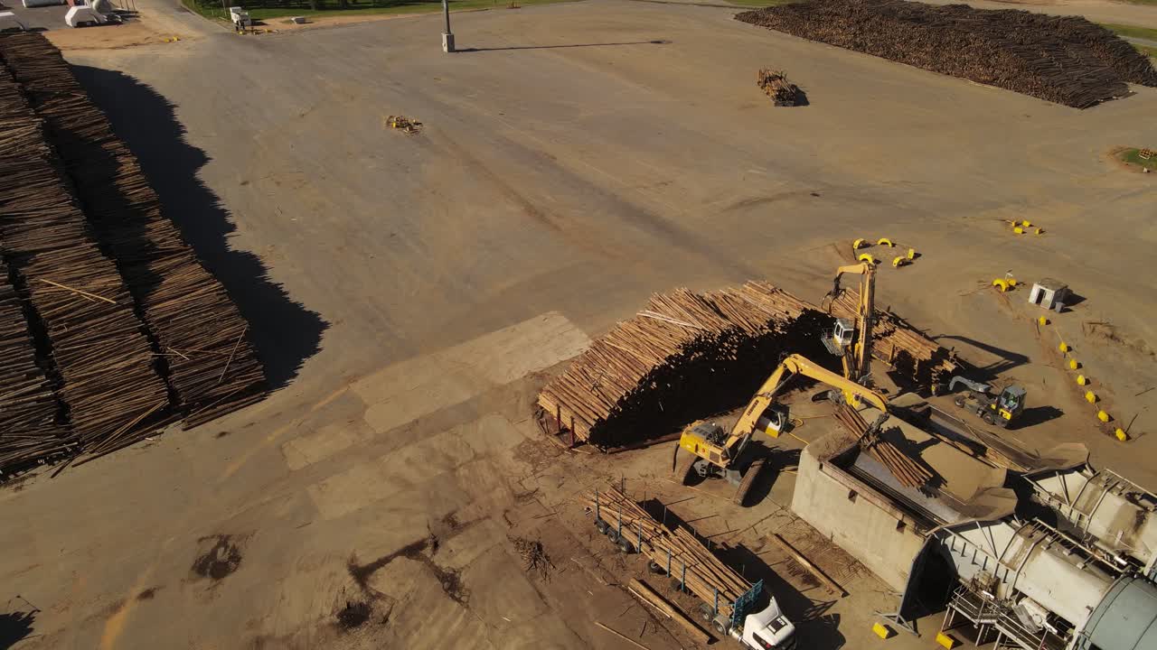Excavator lifts logs in paper mill, rotating aerial view