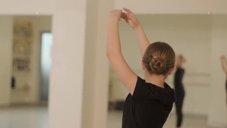 un grupo de jóvenes estudiantes de ballet con ropa de baile negra practicando posiciones en un amplio estudio de ballet con pisos de madera y barras montadas en la pared. expresiones enfocadas y movimientos sincronizados.