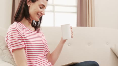 smiling brunette drinking a coffee while watching tablet