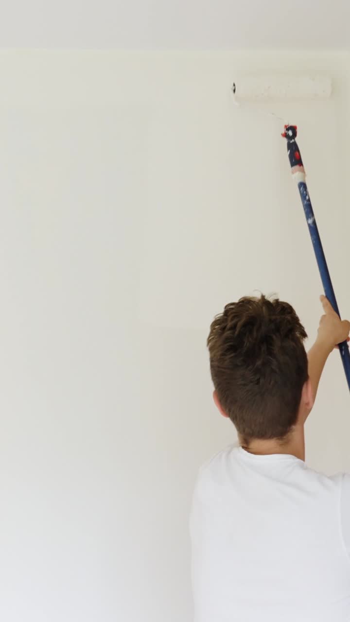 Vertical shot of a young man painting a wall with a roller, DIY project