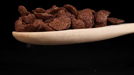 chocolate cereal flakes tumble from a wooden spoon against a black background, captured in slow motion for a dramatic effect