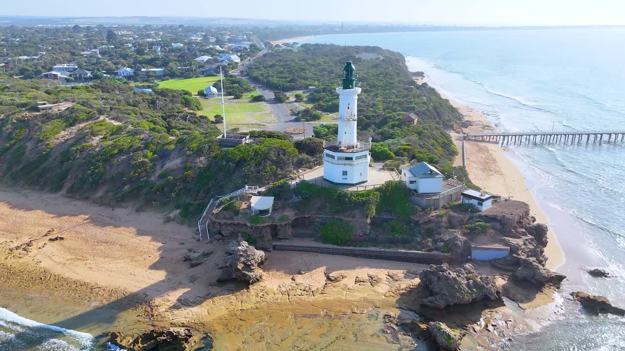 Aerial footage captures Point Lonsdale Lighthouse, surrounded by coastal landscape and ocean, under bright daylight