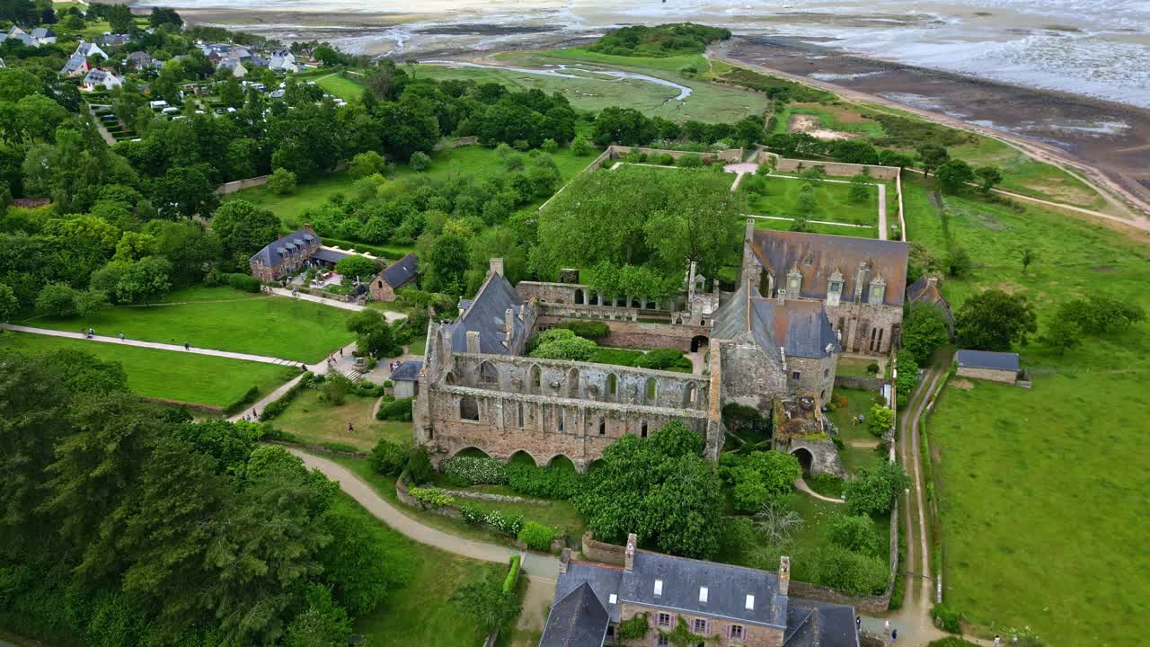 Drone pulls back from Beauport Abbey, showing the sea, beach, and surrounding gardens at Paimpol - France