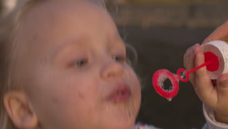 a closeup of a girls face blowing soap bubbles