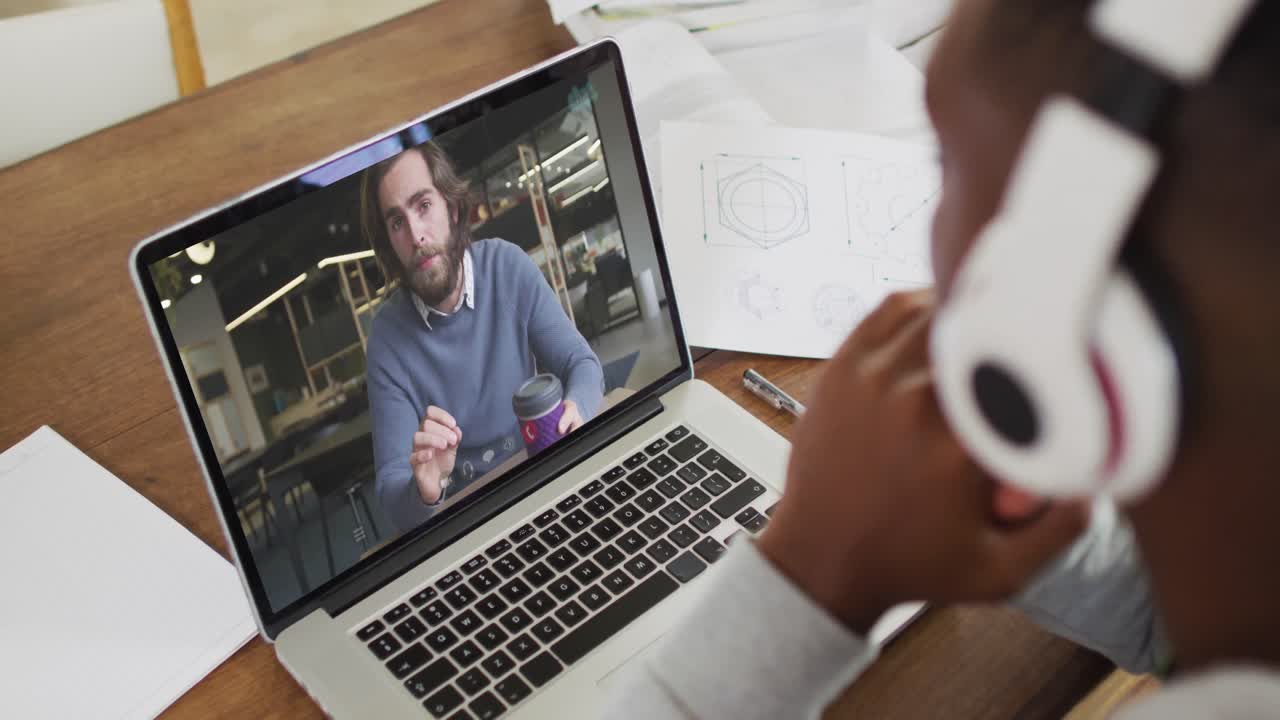African american male college student holding notes while having a video call on laptop at home