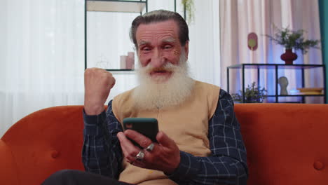 abuelo mayor en casa usar teléfono inteligente escribir navegación, wow sí descubrió gran gran victoria celebrar