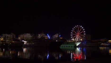 ferris wheel next to yachts in barcelona at night