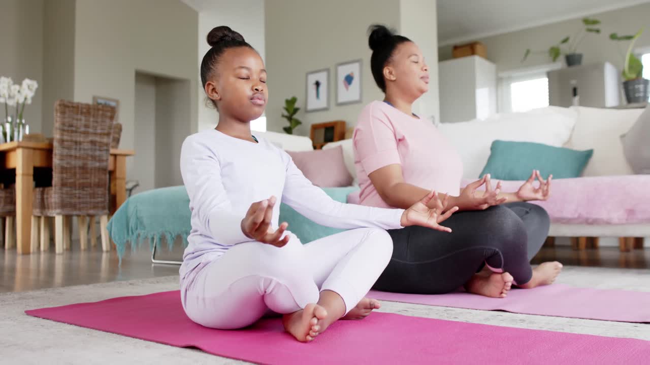 madre e hija afroamericanas felices y inalteradas haciendo meditación de yoga en casa, en cámara lenta