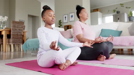 Happy-unaltered-african-american-mother-and-daughter-doing-yoga-meditation-at-home,-in-slow-motion