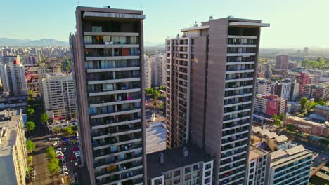 Dolly-in-drone-shot-of-two-identical-and-tall-residential-buildings-unlike-the-surrounding-ones,-Santiago-Chile