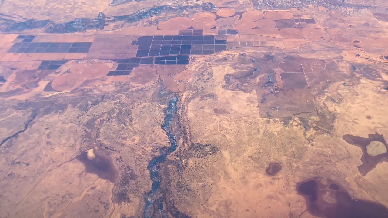 Dramatic aerial footage of landscape from airplane on a sunny day with river, farmland, desert