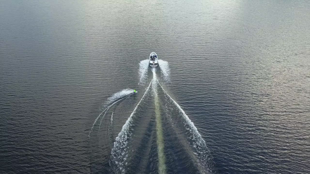 камера следит за катером, на котором вейкбордист прыгает в воду озера