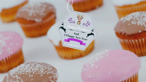 animation of christmas greetings on tag over cupcakes on white background