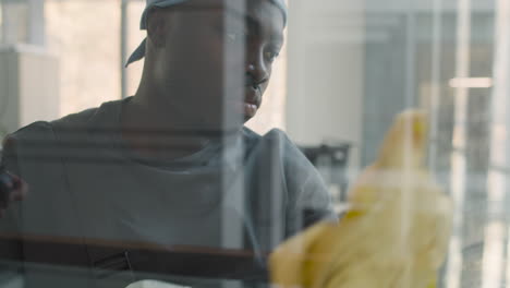 Blick-Von-Außen-Auf-Einen-Putzmann-Mit-Bandana,-Der-Die-Fensterscheiben-In-Einem-Büro-Reinigt