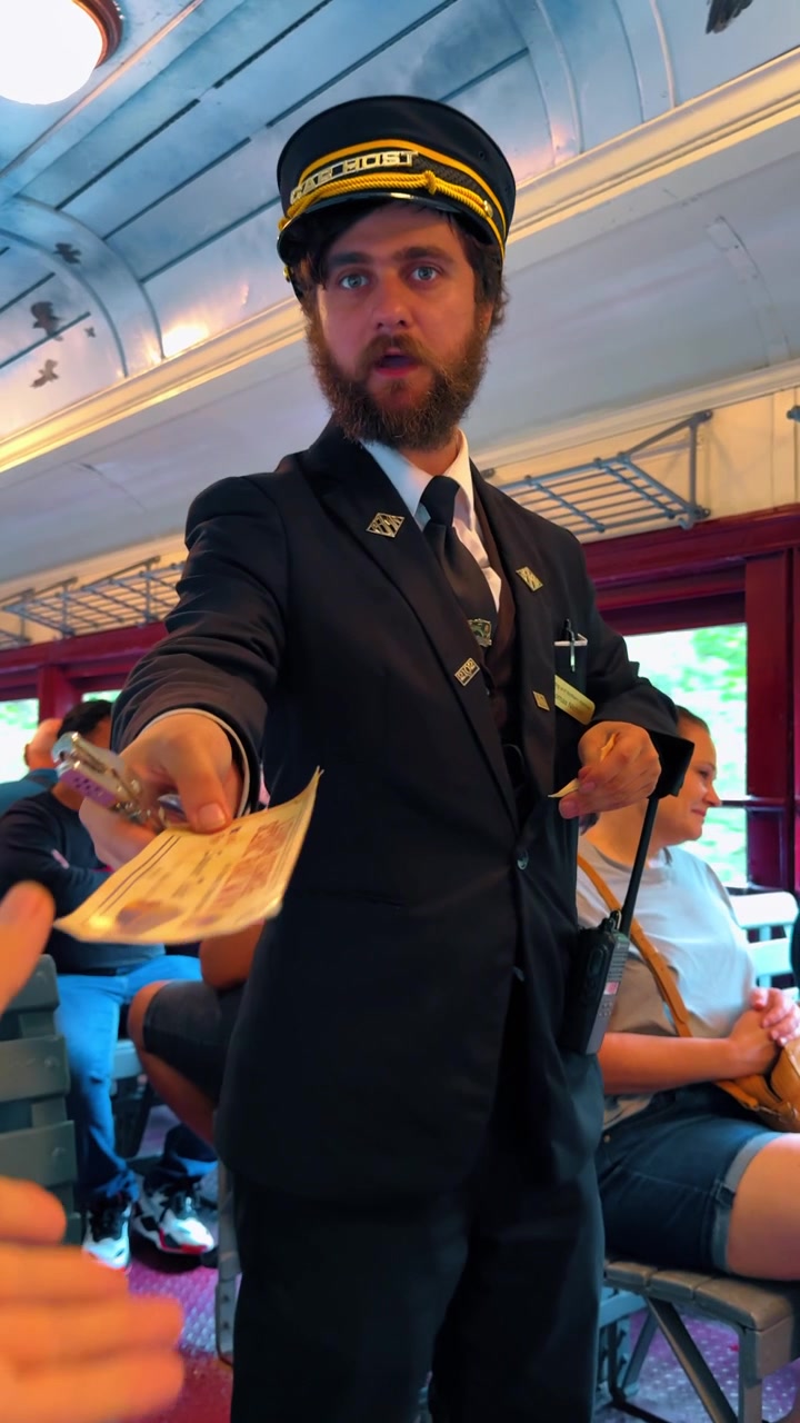 Jim Thorpe, USA, 2 luglio 2025: Persona che tiene in mano biglietti di carta su un treno panoramico d'epoca. Prospettiva in prima persona che tiene due biglietti gialli con un controllore barbuto in uniforme che guarda la telecamera.