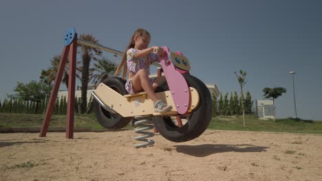 Young-girl-having-fun-playing-on-a-playground-spring-rocker-motorbike