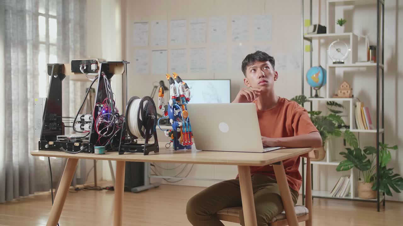 아시아 소년은 집에서 노트북에서 사이보그 손에 대해 생각하고 있습니다.