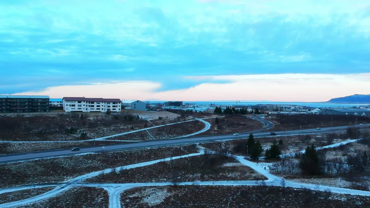 Drone establishing shot of frozen lake Raudavatn, near Reykjavík, Iceland. Camera travels towards highway with busy traffic on a winter day