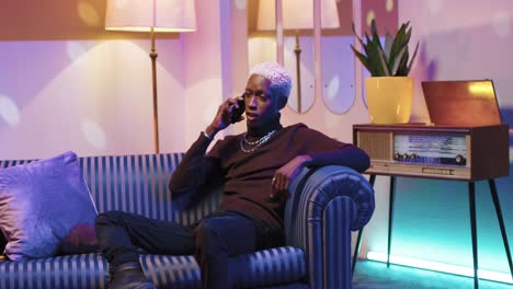 african american man with blonde hair talking on the smartphone while sitting on sofa in a retro room at home