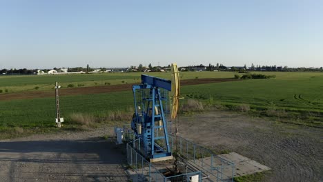 aerial: oil pump at sunset in countryside, old steel pulley extracting oil