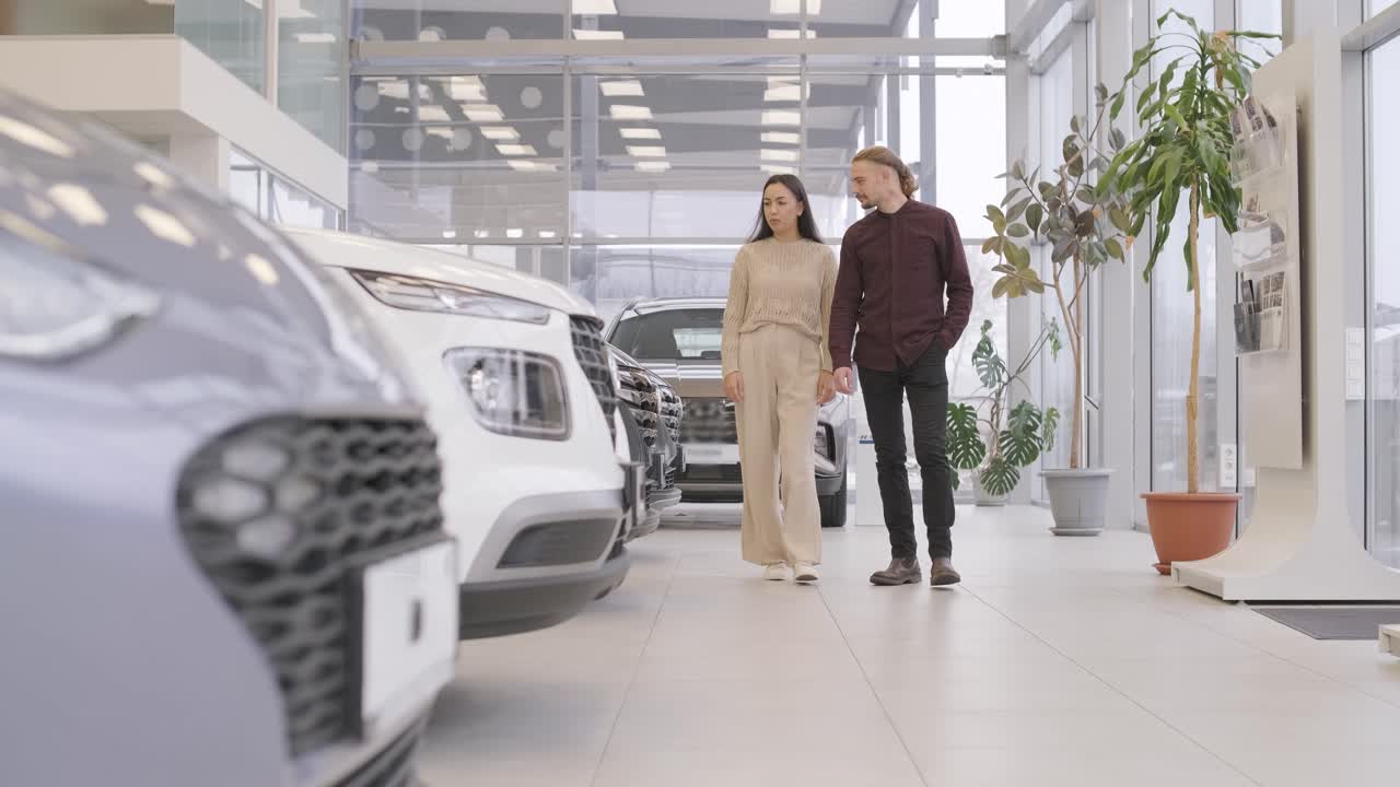 una hermosa pareja de jóvenes en la sala de exposición de automóviles eligiendo un coche nuevo para comprar.
