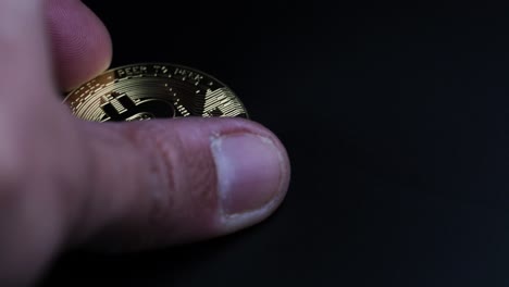 una mano masculina recogiendo bitcoins dorados de un fondo oscuro