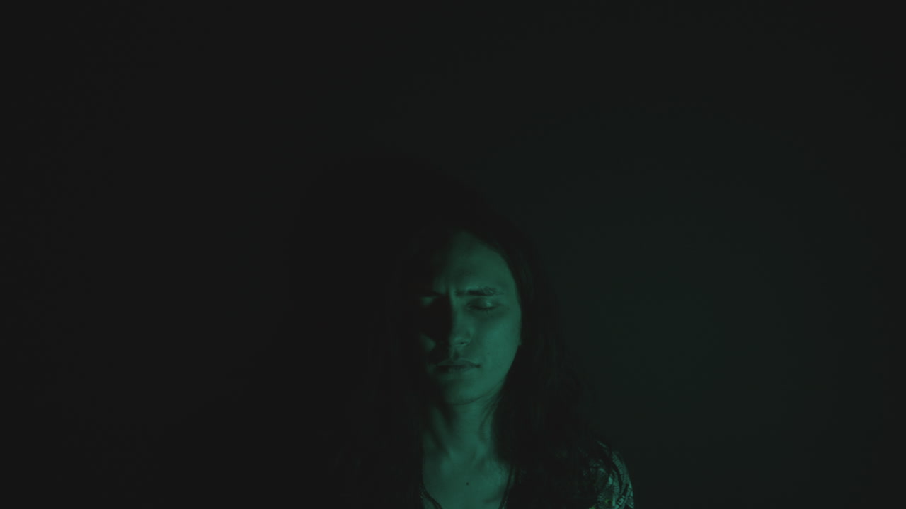 Young Man with Eyes Closed in Dark Studio and Light Projected on Face
