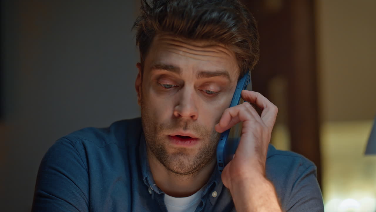 Worried man talking smartphone in dark modern apartment closeup. Frowning guy