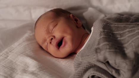 cute newborn baby boy yawning and falling asleep on sofa in living room