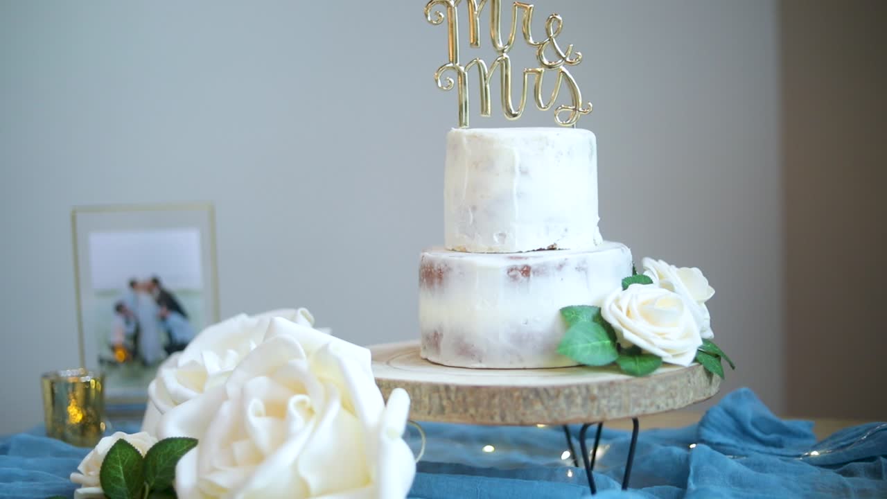 Bolo de casamento simples de duas camadas com cobertura branca decorativa, letras 'Mr e Mrs' e flores brancas para dia de celebração, close-up com zoom