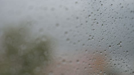 narrow focus view and close-up of rainy glass as rain drops are seen on a window during gloomy and overcast weather