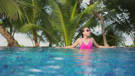 front view of an asian lady in a swimming pool wearing a pink swimwear and sunglasses