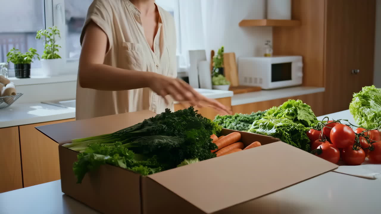 A person unpacking a box of fresh vegetables in a modern kitchen