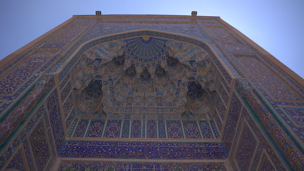 Video con inquadratura dal basso di un iwan islamico ornato, con intricati motivi geometrici a mosaico sul soffitto e facciata piastrellata, un monumento del patrimonio architettonico dell'Asia Centrale e attrazione turistica